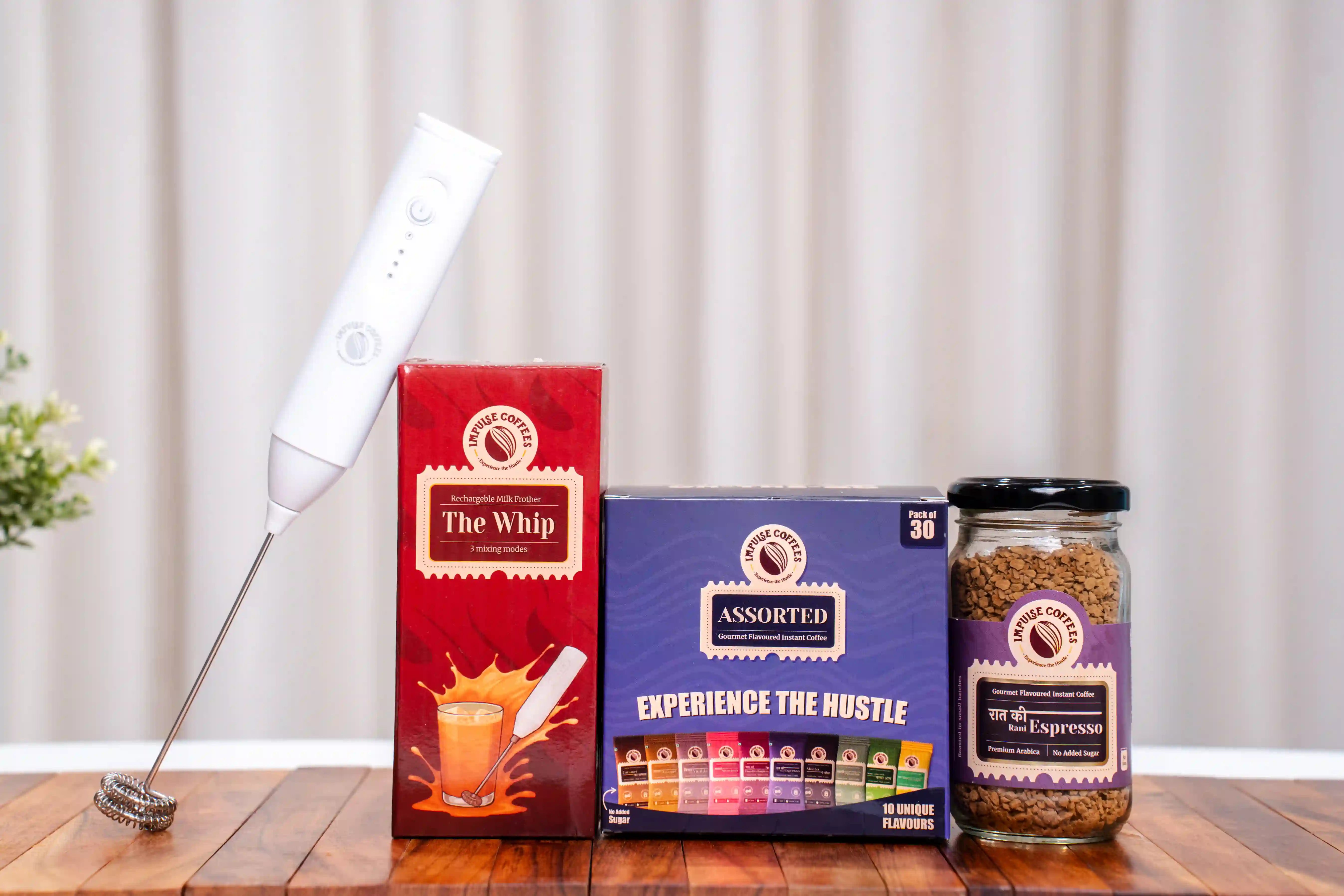 Impulse Coffees Raat Ki Rani Espresso gourmet instant coffee jar, Pack of 30 Assorted Sachets, and The Whip rechargeable milk frother on a wooden table