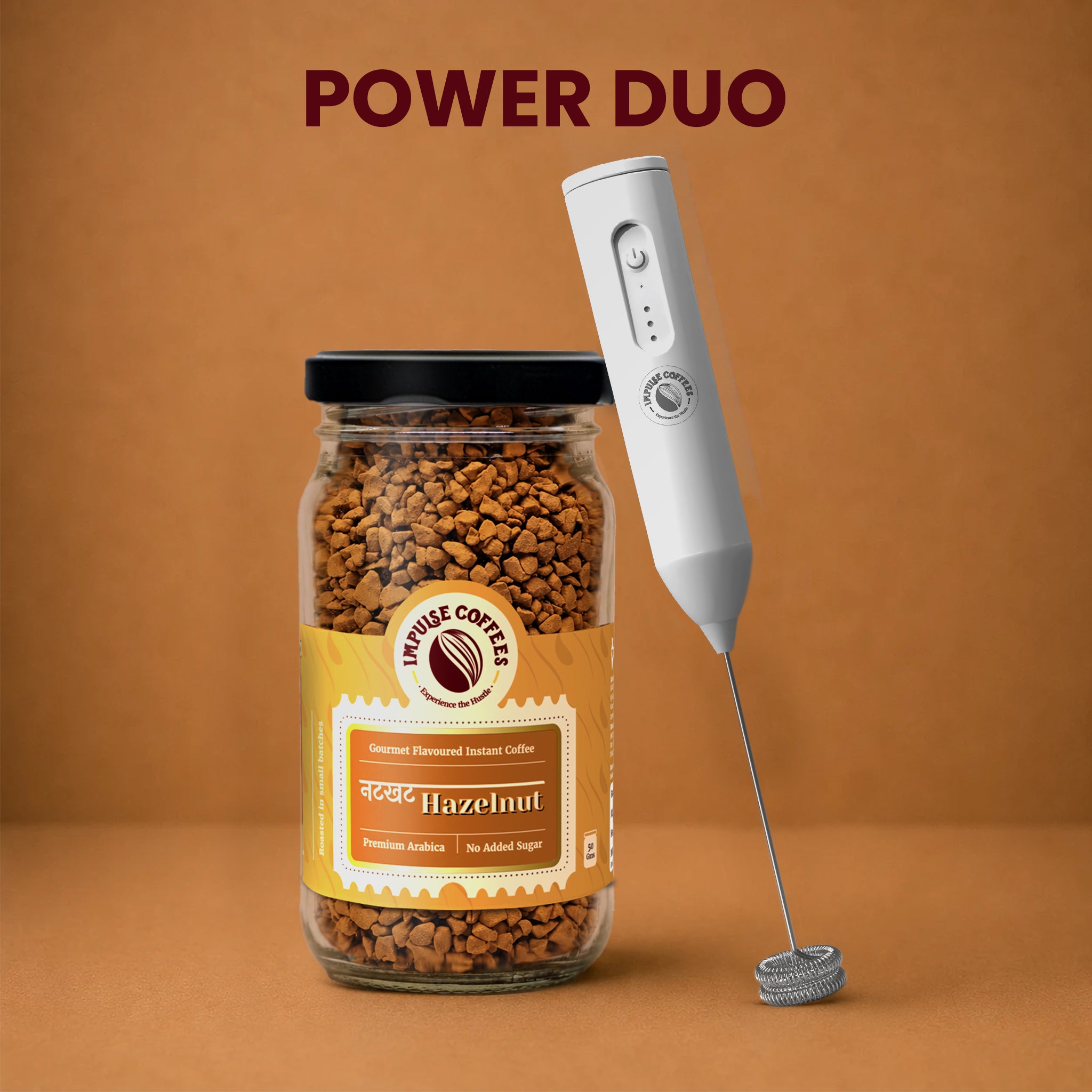 Impulse Coffees Frothy Nut Combo Power Duo bundle showcasing a premium glass jar of Nutkhat Hazelnut gourmet flavoured instant coffee standing next to a white electronic rechargeable milk frother against a warm brown studio background.