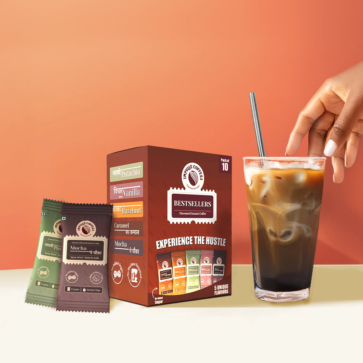 Hand reaching for a glass of iced coffee next to a box of coffee packages by impulse coffees on a peach background