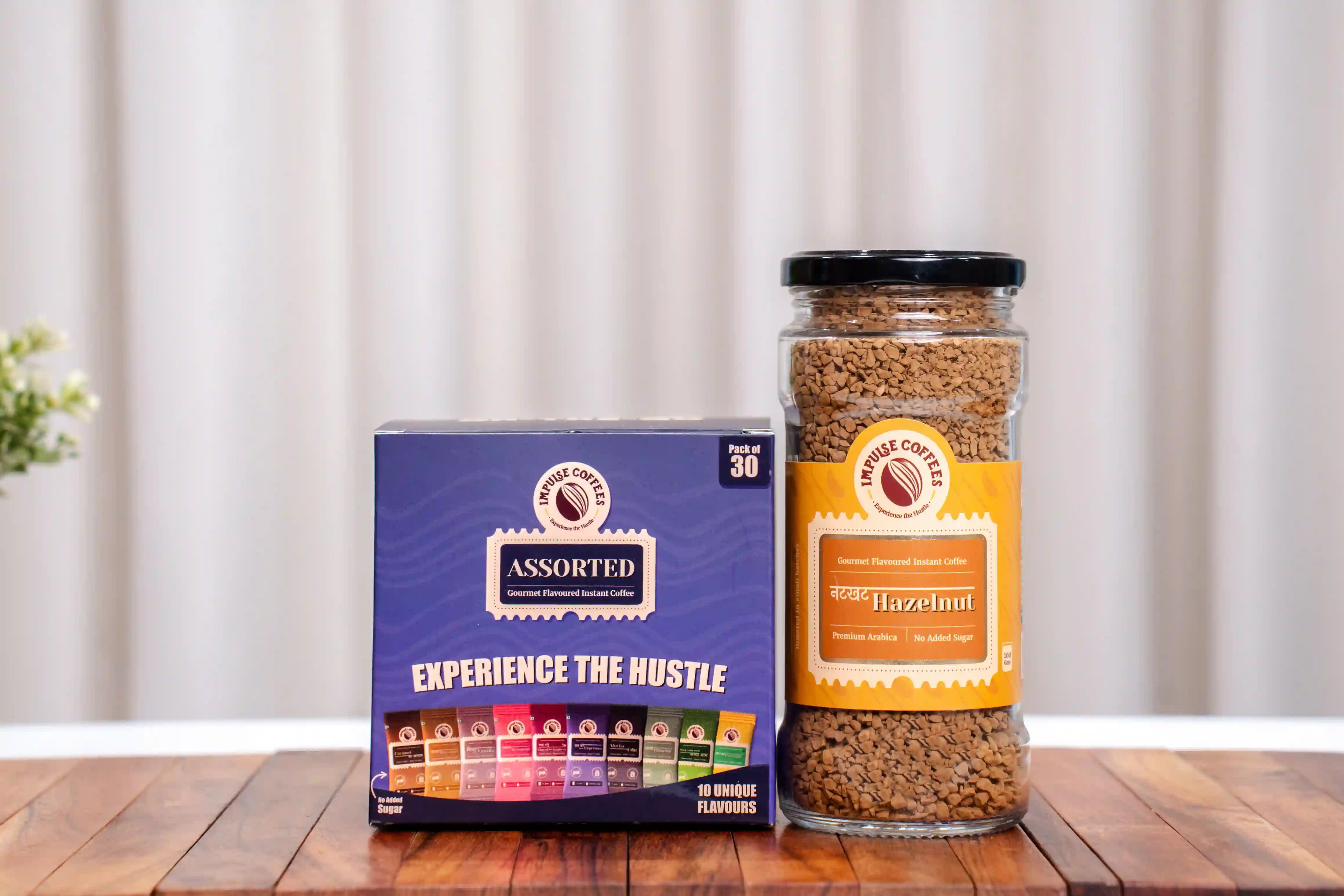 Jar of 10gms Nutkhat Hazelnut and a Assorted Box Pack of 30 labelled 'Assorted Experience the Hustle' on a wooden surface with a white curtain background.