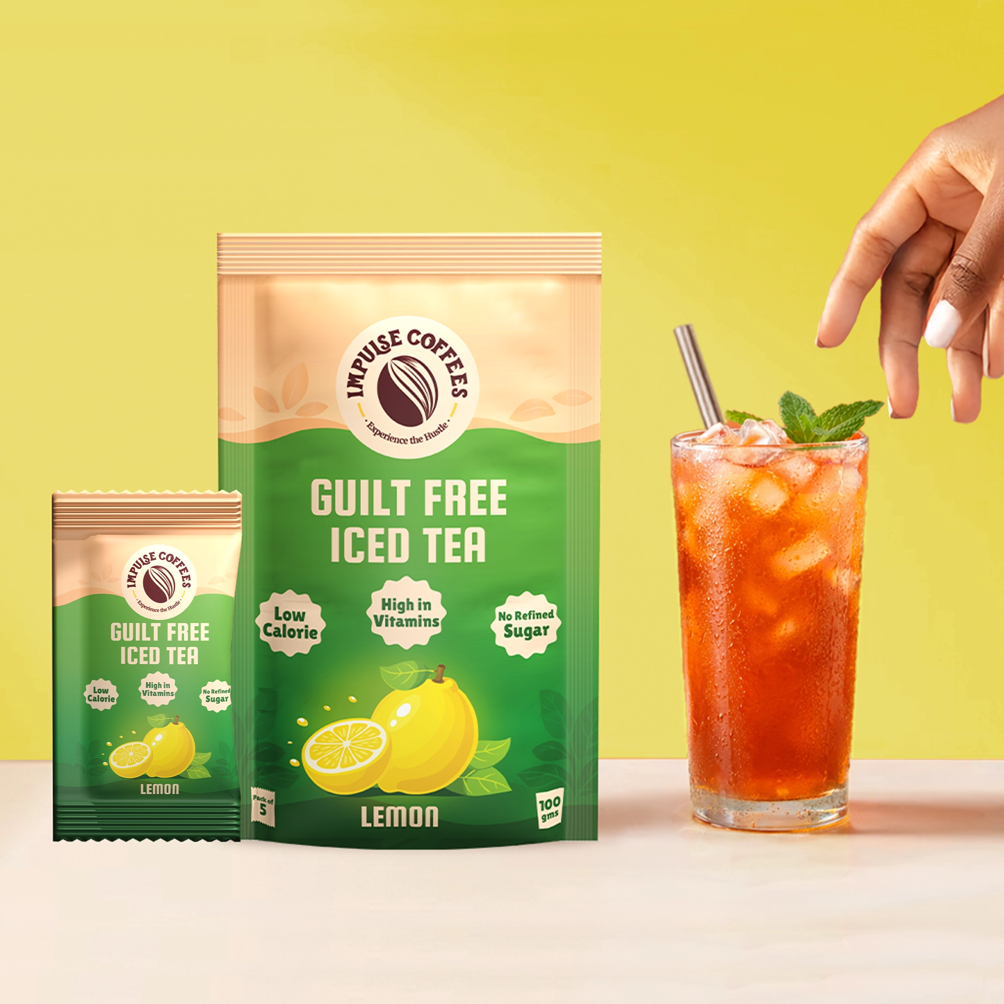 Impulse Coffees Guilt Free Iced Tea in Lemon flavour, displaying a 100g main pouch next to a single sachet and a glass of refreshing iced tea with a steel straw and fresh mint leaves on a bright yellow background.