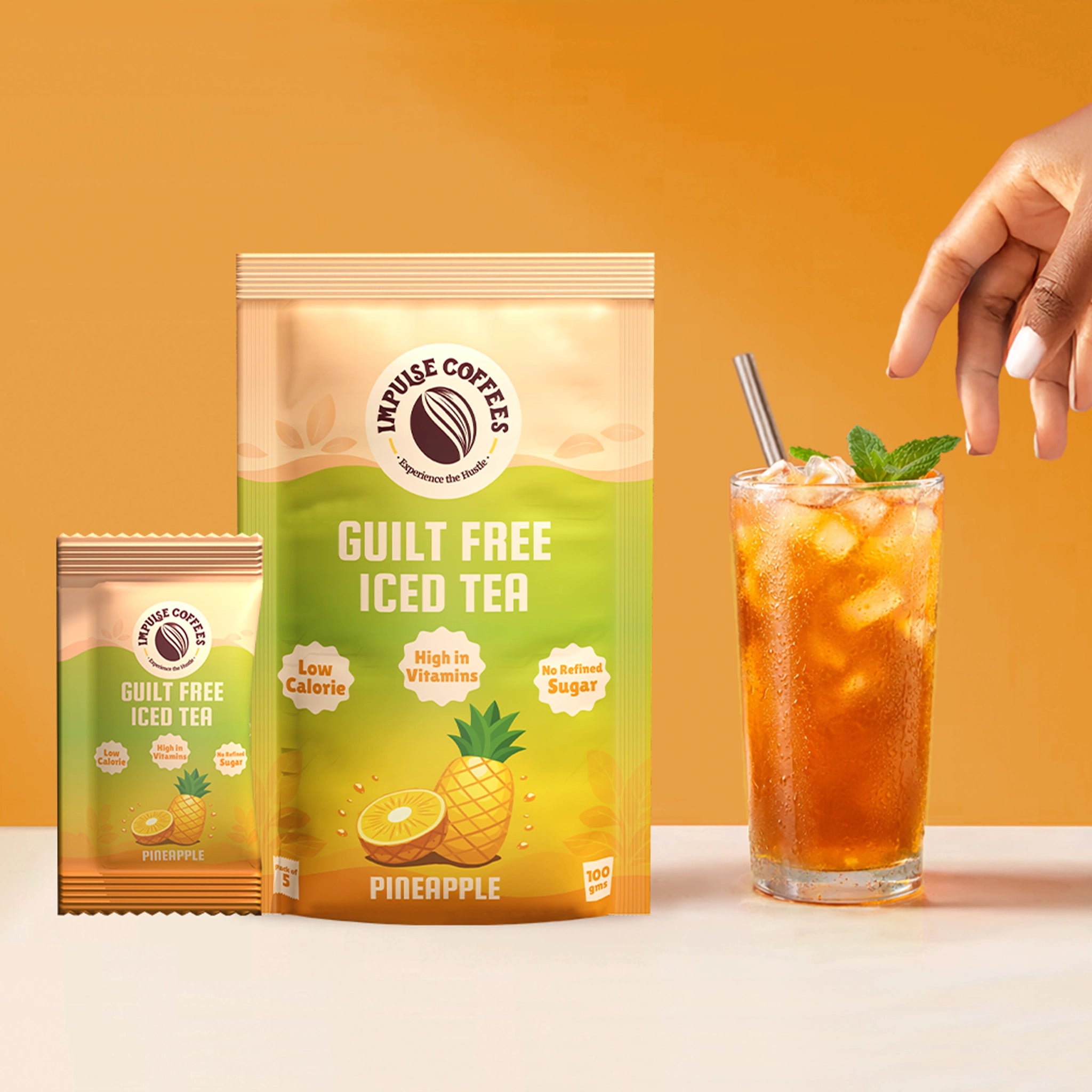 Impulse Coffees Guilt Free Iced Tea in Pineapple flavour, showcasing a 100g stand-up pouch, a single-serve sachet, and a tall glass of iced tea with a steel straw and fresh mint on a vibrant orange and green background.
