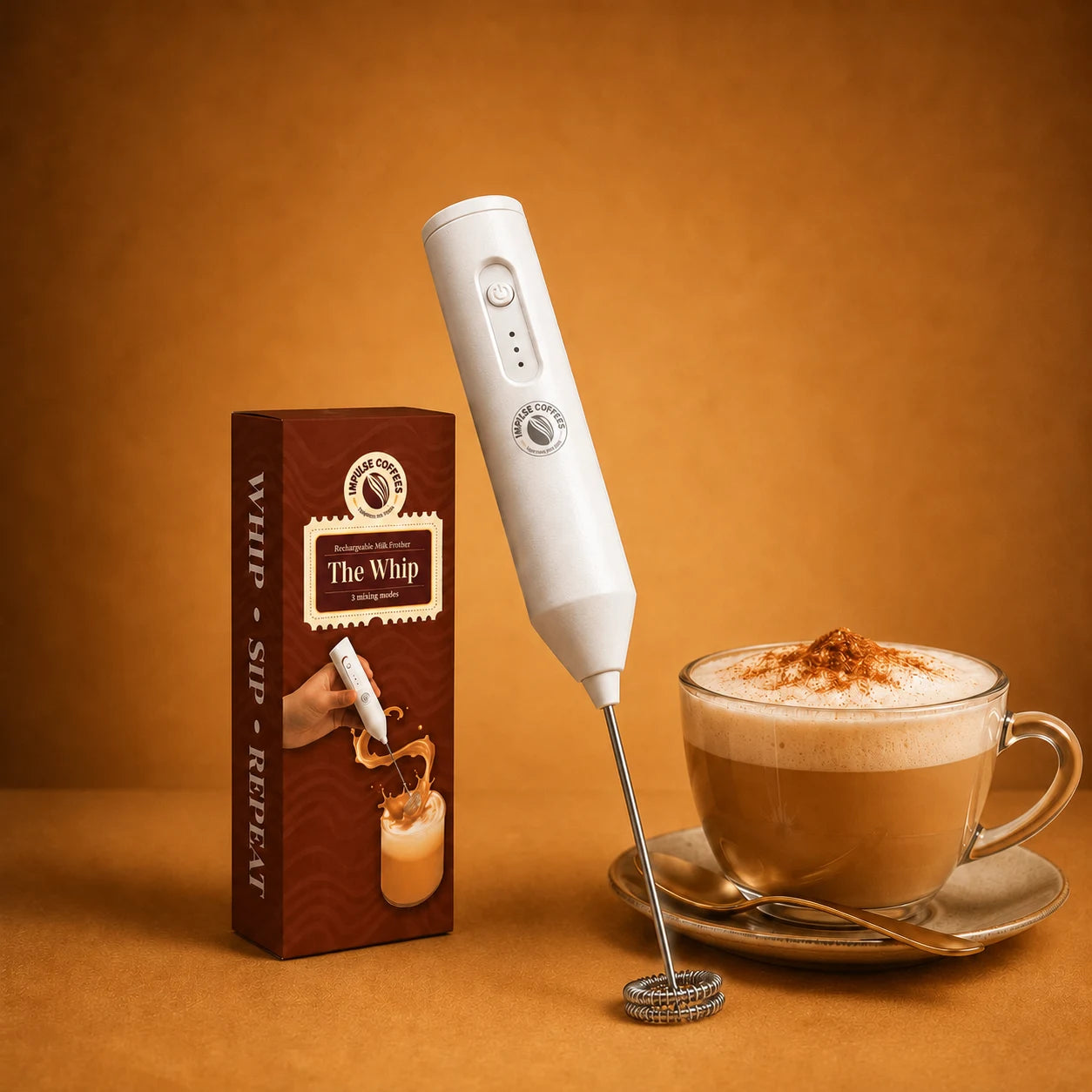 White handheld impulse coffess milk frother with packaging box and a cup of coffee on an orange background
