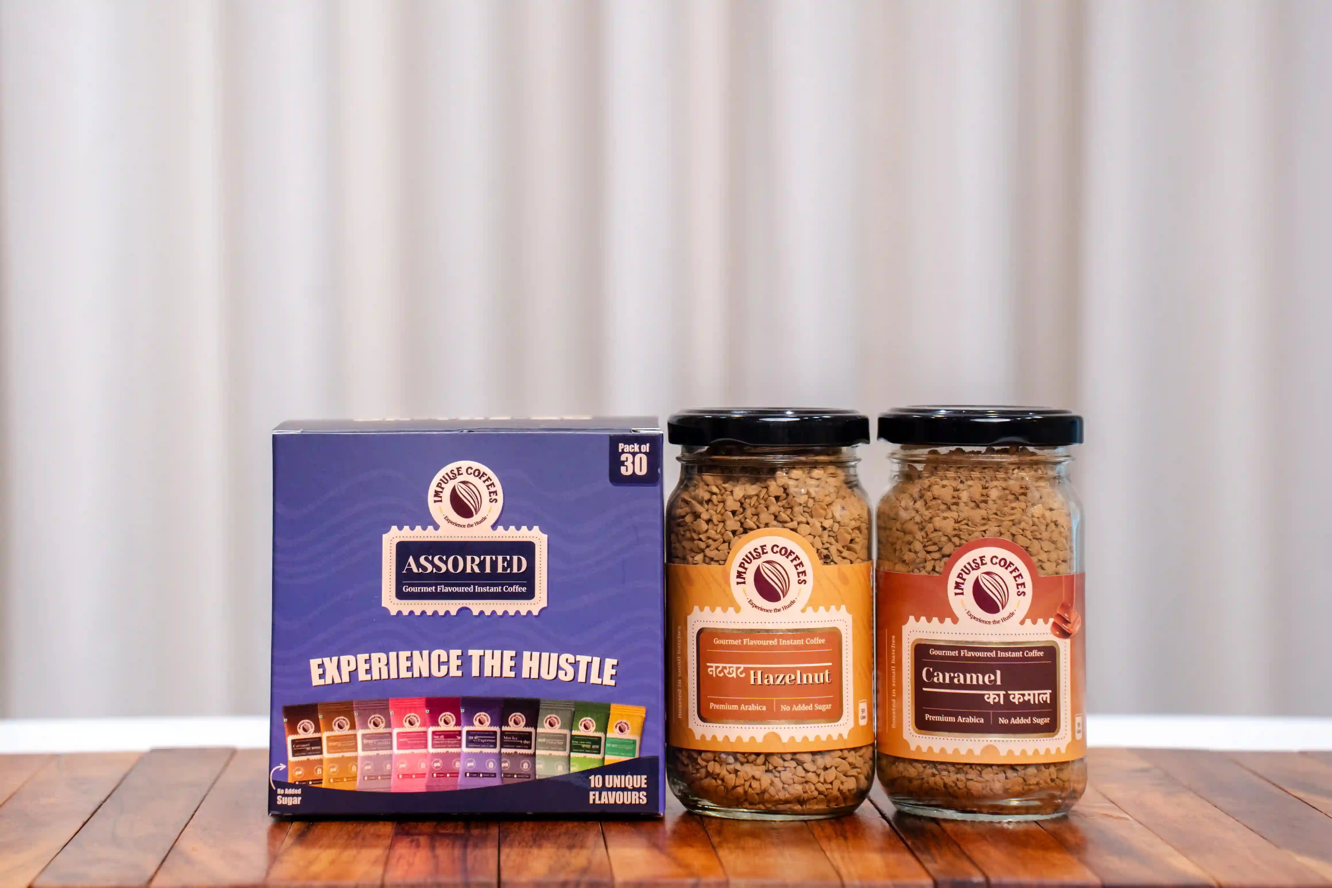 Assorted coffee pack of 30 sachets along with caramel ka kamal and nutkhat hazelnut coffee products on a wooden surface with a neutral background.